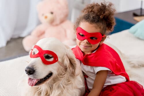 A little girl and her golden retriever in matching super hero costumes.